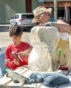 Artist gives hands on trainig in sculpture to a young visitor