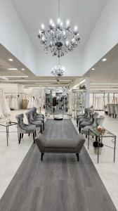 Interior showroom at Trudys Brides with sparkling chandeliers, rows of wedding gowns, plush gray chairs, and a central mirrored fitting area for bridal appointments.