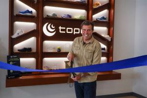 Founder, Tony Post, stands with scissors and a blue ribbon at the official opening of Topo Athletic's new office space.