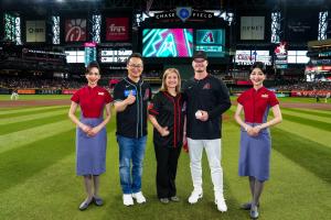 China Airlines President Kevin Chen, Phoenix Mayor Kate Gallego, and Arizona Diamondbacks pitcher Philip Abner stand together on the field at Chase Field, joined by two China Airlines flight attendants in uniform, with the stadium crowd and scoreboard in 