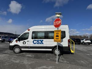 White COAST Autonomous electric Ford E-Transit van branded with CSX logo parked at Selkirk rail yard, equipped with yellow accessibility ramp and safety signage
