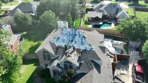 Roofing crew installing new shingles and protective underlayment on a large residential home during a full roof replacement project.