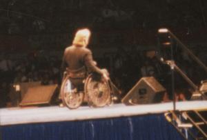 Man in a wheelchair speaking to a crowd of people on a stage.