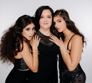 Group photo featuring Farrah and Tamara Mechael with their mother. The sisters wear glamorous black-and-gold stagewear with artistic makeup, while their mother stands in the center in a sleek black dress, representing the family-driven foundation of Scorp