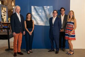 People are posed in front of a prize winning art piece called Book of Hours (Nones). It is a unique, hand-shaped, wall-relief photograph that measures 30” x 40” x 4”. The works feature images of cumulus clouds. After printing the image, Allison wet and ph