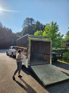 A young woman holding a packet of papers inspects the upper section of a trailer outfitted with a solar microgrid.