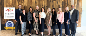 A group of professionals standing together in front of a wooden backdrop, showcasing the St. Johns County Chamber of Commerce logo.