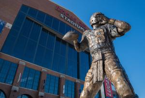 Low-angle photo of a large bronze quarterback statue holding a football,