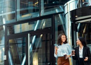 Two business women walking out from commercial glass doors in an office building.