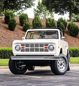 Front view of a Wimbledon White Vintage Modern Classic SUV parked outdoors, showcasing its lifted stance, chrome bumper, and rugged off-road tires.