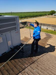 Mechanical Air technician spraying water on an outdoor HVAC unit in Fresno, California, as part of professional maintenance and cleaning services.