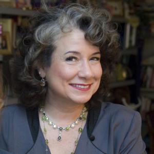 Image of author and professor Gina Barreca shows a woman smiling, wearing a colorful scarf, and expressing humor and happiness.