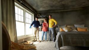 Restoration technician standing with two homeowners in a smoke-stained bedroom, inspecting fire damage on walls and ceiling.