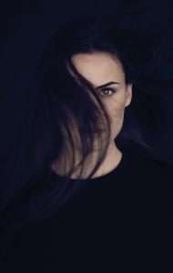 A dark photo of a woman in hiding from a sadistic stalker with her hair partially covering her face.