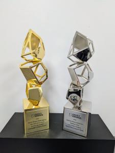 Two Davey Award trophies displayed on a black surface against a white background. The gold trophy on the left is engraved with “Secret Weapon Media Agency – We Help Clients Grow,” while the silver trophy on the right is engraved with “Bankston Motor Homes