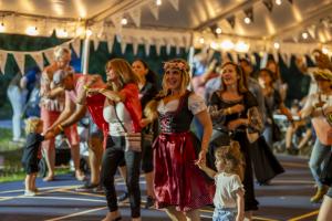 Women in dirndl dresses dancing with families at Oktoberfest Miami under a decorated festival tent.