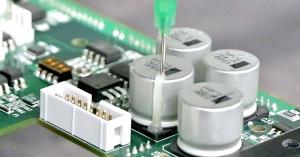 Dymax 9773 low-outgassing adhesive is dispensed onto PCB components to ruggedize them.
