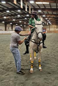 an arena polo player gets help adjusting his stirrups