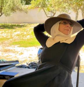 sister kate in a sun hat sitting back waiting, on a veranda under a portico