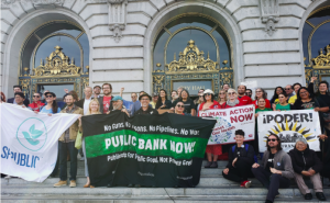 People hold pro-public bank banners on the steps of SF City Hall with smiling faces.