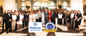 A large group of Hilton Dubai Palm Jumeirah staff pose together in the hotel lobby to celebrate earning the Certified Autism Center™ (CAC) designation, with Hilton and IBCCES CAC logos displayed in front.