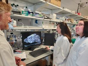 Three scientists in white lab coats examining an image of a mouse brain on a computer monitor