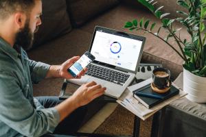 This image shows the web platform www.chaia.io in use by a man holding his phone and using his laptop. He is looking at the coins details page on his phone and analysis cryptocurrencies on his laptop.