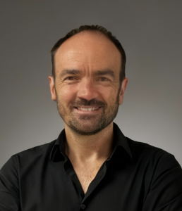 Portrait of David Douilet, newly appointed Director of Consumer Sales at Peli Products. David is smiling, wearing a black shirt, and standing against a neutral grey background.