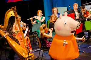 Peppa Pig engages with a colorful orchestra playing various instruments, creating a lively and whimsical atmosphere on stage.