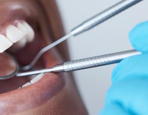 Woman with her mouth open next to a gloved hand holding dental tools.