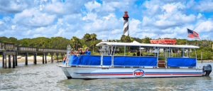 A tour boat named "Fury" glides on water near a striped lighthouse, with a group of people enjoying the scenic view under a blue sky.