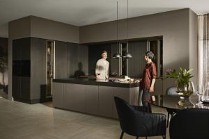 Contemporary German kitchen with grooved dark oak cabinets, bronze glass display, large island, and two people talking.