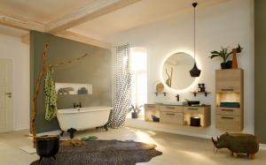 Modern bathroom with floating oak vanity, round backlit mirror, pendant light, and claw-foot tub in soft green and wood tones.