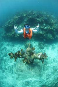 key largo fl underwater view showing a snorkeler in a life vest floating above the moss-covered, bronze Christ of the Abyss statue, with both the person and the statue having their arms raised toward the surface.