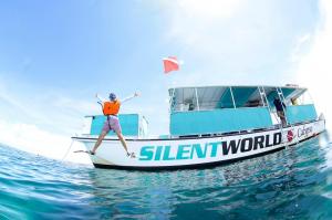 Action shot of a snorkeler in an orange life vest leaping happily from the side of the teal and white Silent World Calypso, a 51-foot Corinthian catamaran, into clear, shallow Key Largo water.