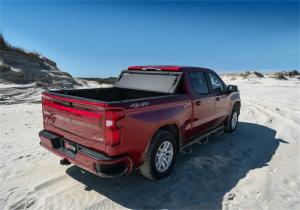 Red pickup truck with a premium tonneau cover parked on a sandy beach, highlighting truck bed protection and sleek design
