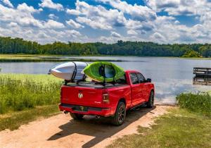 Red pickup truck equipped with a premium tonneau cover carrying kayaks near a scenic lake under a blue sky