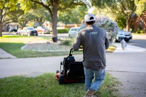 Cerv employee in uniform facing away from camera mowing lawn.