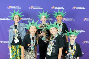 Six students are displaying the trophy they earned for finishing first at the Destination Imagination Global Finals. Representing New York, all are wearing foam “Statue of Liberty” crowns with 'New York' printed on them.