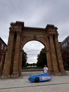 Aaron Novinger standing in front of the Union Station Arch in Columbus next to his bright blue velomobile during his 2,000-mile charity ride, “Pedaling Against Ponzi’s,” to support victims of financial fraud.