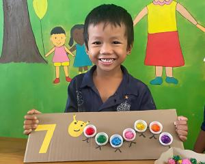 Smiling Cambodian boy holds a handmade counting activity made from bottle caps and pom-poms at Love Without Boundaries’ Early Childhood Development Center.