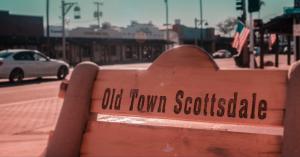 Bench engraved “Old Town Scottsdale” with shops, cars, and street activity in the background.