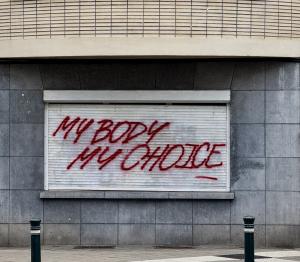 A red graffiti reading “MY BODY MY CHOICE” sprayed across a closed metal shutter. Conceptual photograph by Grace Shi exploring language, control, and resistance.