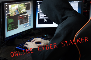 Stalker sitting in a dark room with two computer screens stalking a woman in business.