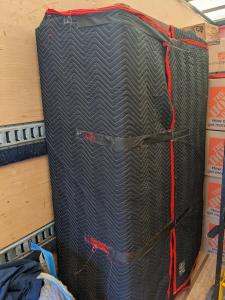 A large piece of furniture inside a moving truck is securely wrapped in black and red quilted moving blankets, ready for transport.