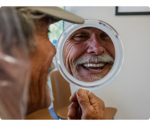 Man with a moustach smiling into a hand mirror