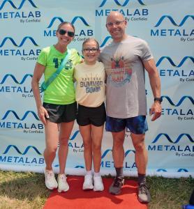 Mike DeAngelo, owner of CrossFit Factory Square in Southington, Connecticut, stands with his family in front of the MetaLab by Confidia backdrop during the Factory Summer Slam event.