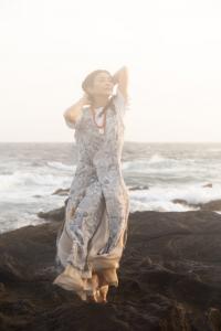 Lady in ethereal dress on the rocks by the sea.