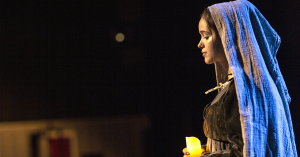 A woman in a blue dress gently holds a candle, creating a serene atmosphere with its flickering light.
