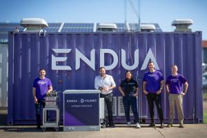 Five smiling businesspeople pose outside of a large purple industrial container labeled "Endua"